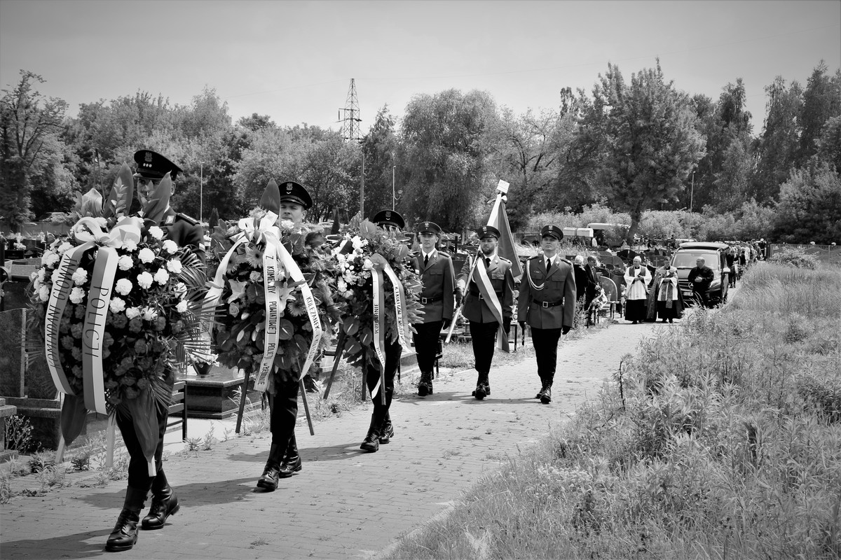 Na zdjęciu widzimy utworzony kondukt na cmentarzu, na czele z umundurowanymi policjantami, którzy niosą wieńce. 