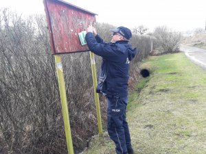 Policjant przyczepia ulotkę informacyjną na tablicy ogłoszeń