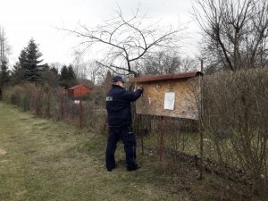 Policjant przyczepia ulotkę informacyjną na tablicy ogłoszeń