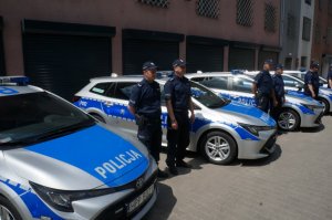 Policjanci stojący obok nowoczesnych radiowozów