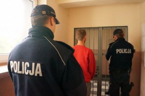 Mężczyzna doprowadzony przez policjantów do pomieszczenia dla zatrzymanych