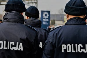 Grupa policjantów stojąca tyłem, widok na miejsce uroczystości.