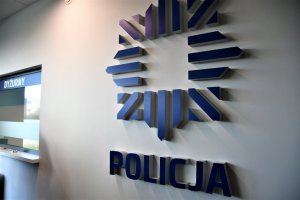 Widok na dyżurkę oraz logo policji znajdujące się na ścianie.