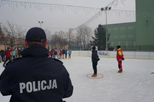 Policjant stojący tyłem na tle bawiących się dzieci