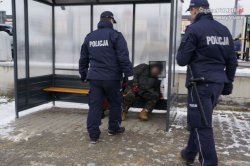 Dwaj policjanci rozmawiają z mężczyną siedzącym na przystanku autobusowym