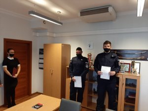 Ślubujący policjanci stoją z aktami ślubowania