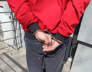 Zdjęcie przedstawia jednego z zatrzymanych mężczyzn, który ma kajdanki założone na ręce trzymane z tyłu.