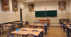 Zdjęcie przedstawia pustą salę lekcyjną przygotowaną do matury. Na zdjęciu widoczne są:  tablica lekcyjna, puste ławki z krzesłami z wydzielonymi stanowiskami dla uczniów.