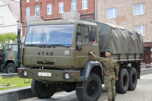 Zdjęcie przedstawia pojazd wojskowy oraz trzymającego drzwi żołnierza.