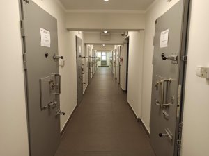 Zdjęcie przedstawia podłużny korytarz. Po prawej i lewej stronie znajdują się cele dla osób zatrzymanych