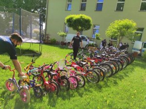 Policjant ustawiający rowery przed domem dziecka, po lewej stronie drugi policjant zmierzający w kierunku dzieci stojących przy radiowozie..