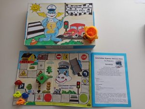 Zdjęcie przedstawia grę edukacyjną &quot;Samochodowe wyprawy Smoczycy Klary&quot;  z planszą, wykonanymi ręcznie elementami gry oraz zasadami gry i pudełkiem.