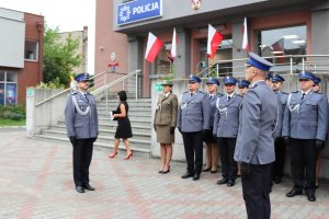 Policjanci na drugim planie stoją w szyku przed budynkiem będzińskiej komendy. Na pierwszym planie, dowódca uroczystości składa meldunek Zastępcy Komendanta Wojewódzkiego Policji w Katowicach o gotowości policjantów do przystąpienia do uroczystości.