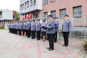 Na pierwszym planie Komendant Powiatowy Policji w Będzinie, który wita zebranych gości i przemawia do nich. Na drugim planie policjanci ustawieni w szyku przed budynkiem będzińskiej komendy.