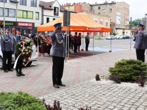 Na pierwszym planie oddawanie honoru przez Zastępce Komendanta Wojewódzkiego Policji w Katowicach insp. Dominika Łączyka podczas składania wieńca od Komendanta Głównego Policji. Za Zastępcą Komendanta Wojewódzkiego znajduje się wieńcowy trzymający wieniec od pracowników będzińskiej komendy, za nim znajduje się Komendant Powiatowy Policji w Będzinie insp. Arkadiusz Więcek.