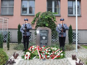 Dwóch policjantów stojących przy obelisku &amp;quot;Poległym w służbie ojczyźnie&amp;quot; oraz złożone kwiaty przed obeliskiem.