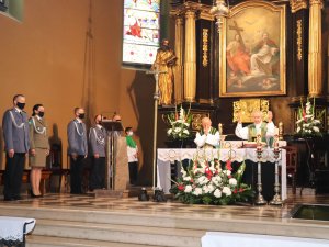 Uczestnicy liturgii. Policjanci i funkcjonariuszka straży granicznej znajdują się po lewej stronie patrząc na ołtarz. Księża odprawiają Mszę Świętą przed ołtarzem.