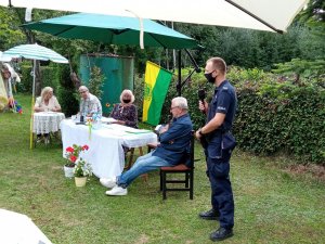 Dzielnicowy zabierający głos podczas spotkania z działkowcami na terenie ogródków działkowych.