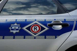 Na zdjęciu przedstawiona częściowo lewa strona radiowozu policyjnego, gdzie widoczne są emblematy odznaki policyjnej oraz symbolu wydziału ruchu drogowego.