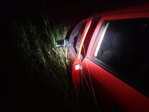 Zdjęcie przedstawia fragment czerwonego pojazdu z lewej strony, który stoi w polach po zmroku.