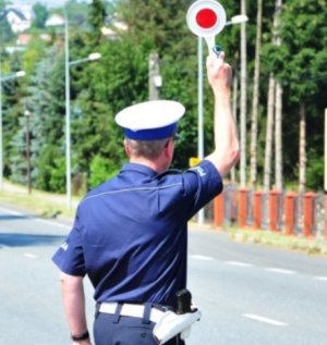 Umundurowany policjant trzymający w ręku tarczę do zatrzymywania pojazdów.