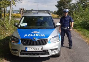 Umundurowany policjant drogówki stojący obok radiowozu.