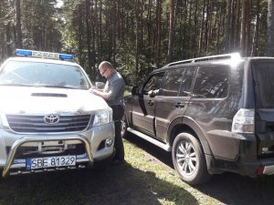 Na zdjęciu widoczny strażnik leśny stojący między swoim pojazdem służbowym oraz samochodem cywilnym podczas wykonywania czynności.