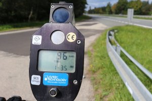 Policyjne urządzenie pomiarowe do pomiaru prędkości wskazujące na ekranie 96km/h. W tle znajduje się droga.