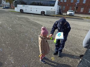 Policjantka zakładająca dziewczynce odblask na rękę.