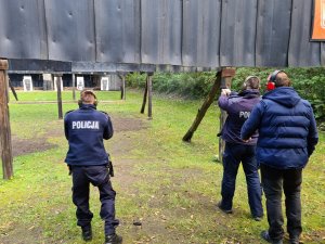 Policjanci strzelający na strzelnicy. Za policjantami stoi instruktor.