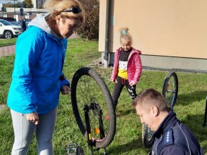 Policjant grawerujący rower. Obok niego kobieta i dziewczynka.