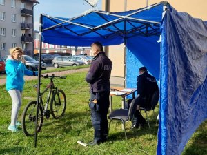 Policjanci znajdujący się w niebieskim namiocie, Przed nimi stoi kobieta trzymająca rower.