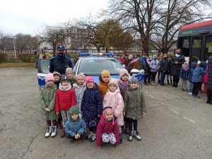 Grupa dzieci stojąca przy umundurowanej policjantce przed policyjnym radiowozem.