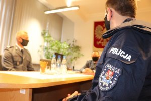 Na pierwszym planie widoczny lewy profil umundurowanego policjanta, w oddali widoczni Komendant Powiatowy Policji w Będzinie i Komendant Komisariatu Policji w Będzinie