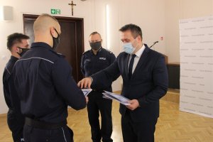 Starosta Będziński wręcza policjantowi list gratulacyjny oraz bon upominkowy. Na zdjęciu znajdują się jeszcze dwaj nieumundurowani policjanci, na czele z Komendantem Powiatowym Policji w Będzinie.