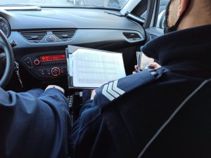 Policjant w radiowozie wraz z listą osób na kwarantannie podczas kontroli.