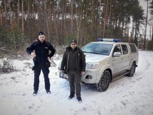 Stojący policjant i strażnik leśny przed samochodem straży leśnej.