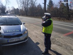 Policjant stojący obok radiowozu przy drodze z urządzeniem pomiarowym mierzącym prędkość.