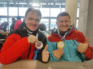 Dwóch nieumundurowanych policjantów trzymających medale za osiągnięcia w alpejskich zawodach narciarskich.