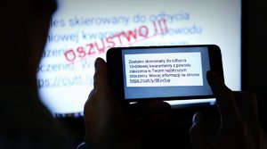 Na pierwszym planie zdjęcia widzimy telefon komórkowy trzymany w rękach z wyświetlającym się napisem stworzonym przez oszustów o obowiązku 10 dniowej kwarantanny.