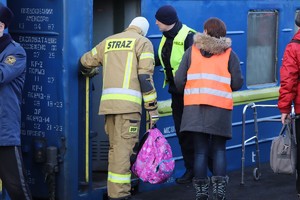 Policjant i strażak stoją przy wyjściu z wagonu pociągu pomagając wysiadającym osobom.