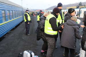 Na pierwszym planie policjant pomagający starszej Pani iśc, na zdjęciu znajdują się również inne osoby, które wysiadły z pociągu oraz policjant i przedstawiciele straży miejskiej.