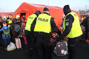 Policjanci pomagają w niesieniu bagaży kobietom z dziećmi.