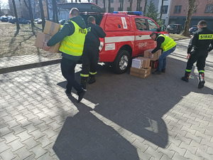 Policjanci i strażacy, którzy pakują do samochodu kartony z rzeczami.