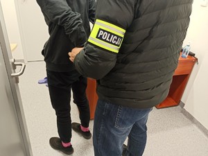 Policjant pionu kryminalnego zakładający kajdanki zatrzymanemu.