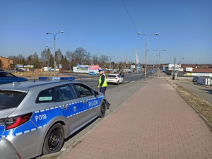 Policjant przy radiowozie wychodzący na jezdnię w celu zatrzymania pojazdu.