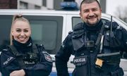 Dwoje umundurowanych policjantów stoi przed radiowozem