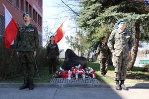 Grupa młodzieży przebrana w mundurach stoi przy grobie, ku pamięci policjantów II RP zamordowanych przez NKWD w 1940 roku stanowiąc wartę honorową.