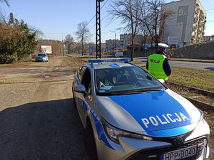 Policjant drogówki stojący przy samochodzie i obserwujący drogę.