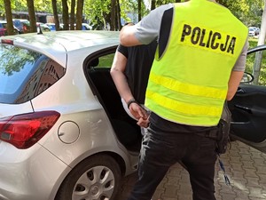 Policjant umieszczający zatrzymanego w samochodzie.